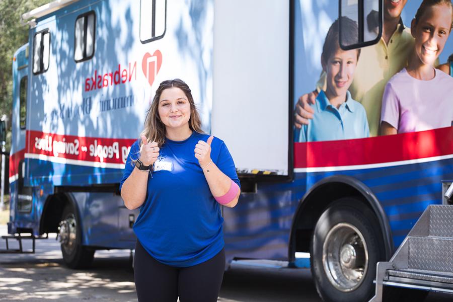 Olivia Lohrenz gives two thumbs up after donating blood. She has a pink bandage wrapped around her elbow. 